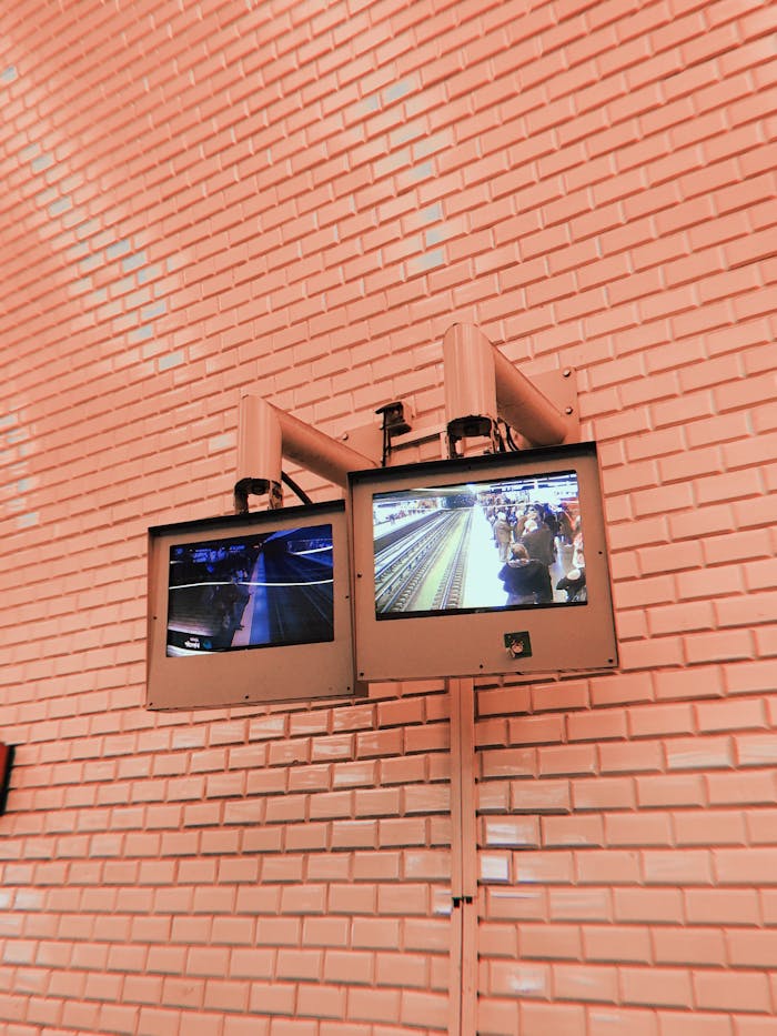 Dual monitors on a brick wall display subway surveillance footage.